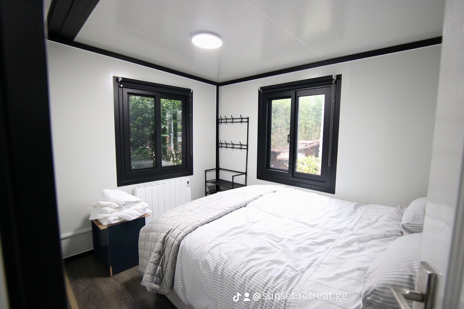 Bedroom with the bed made up, two windows and a hanging rail