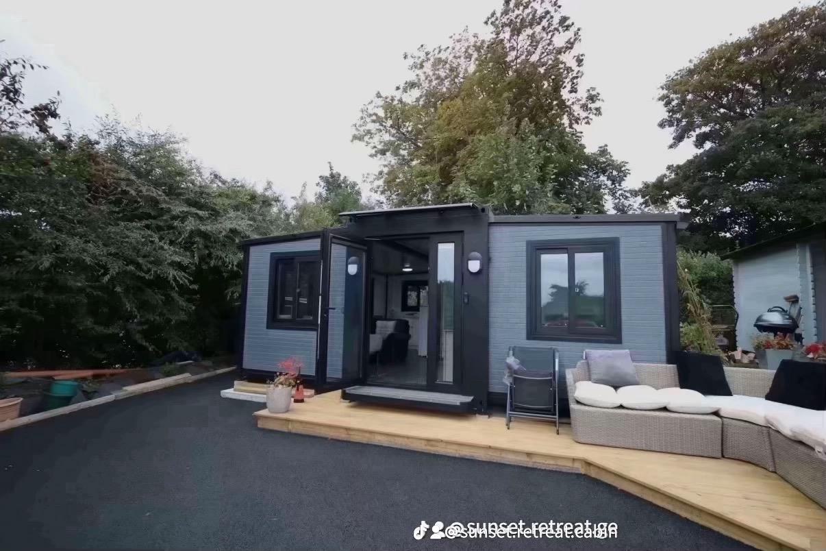 The grey cabin in daylight with its doors open onto the wooden deck and outdoor seating